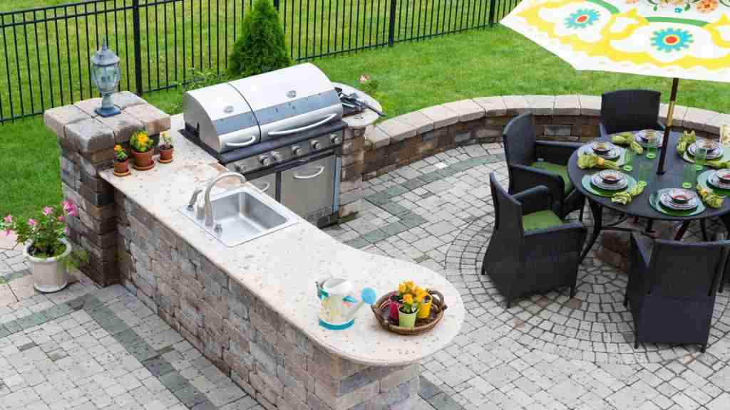 Outdoor kitchen with a stone island, sink, grill, and furnished backyard patio