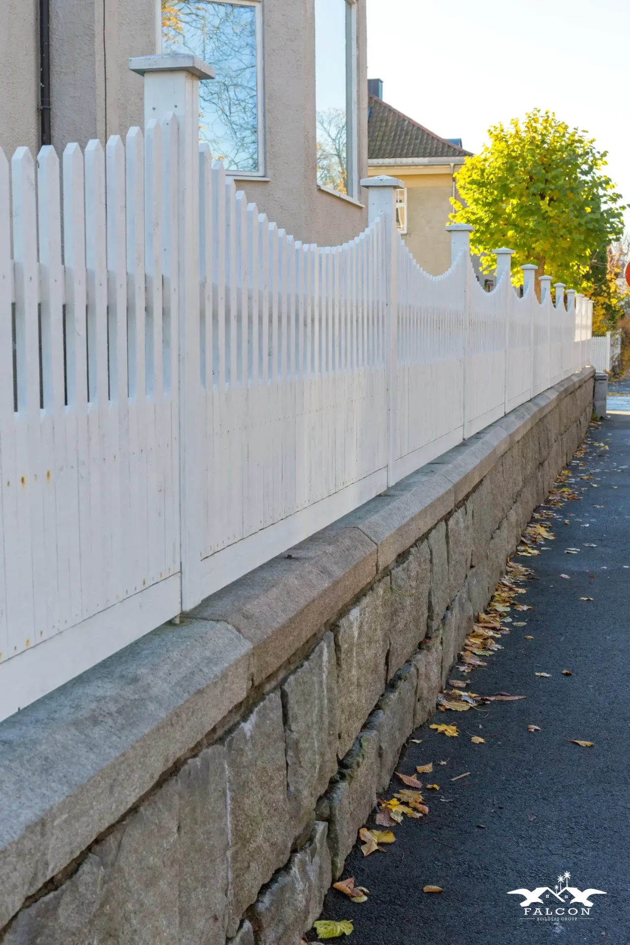 Residential fence installation featuring classic white picket privacy fence mounted on stone base along suburban property line.