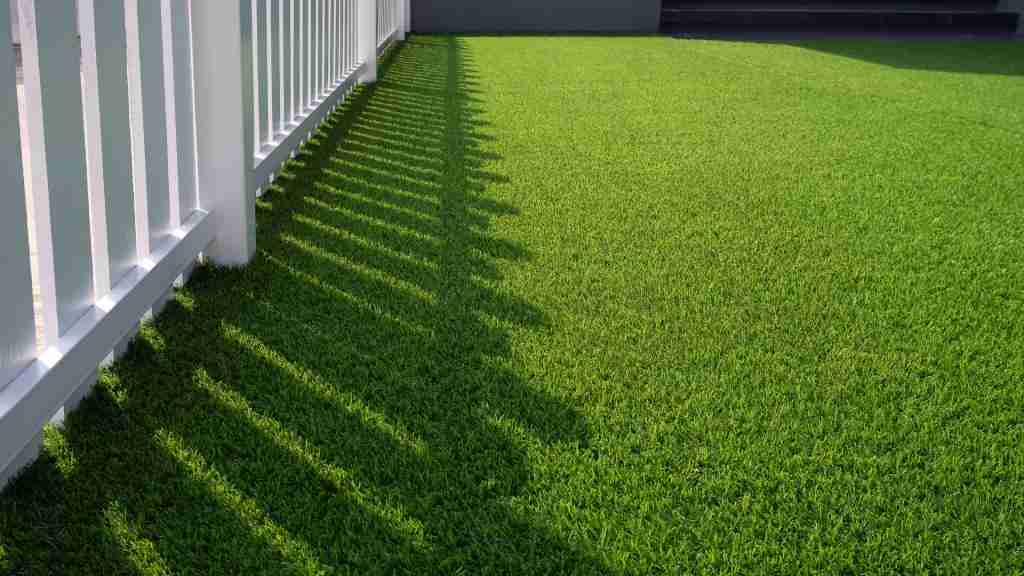 Artificial grass installation in a backyard with clean white fencing